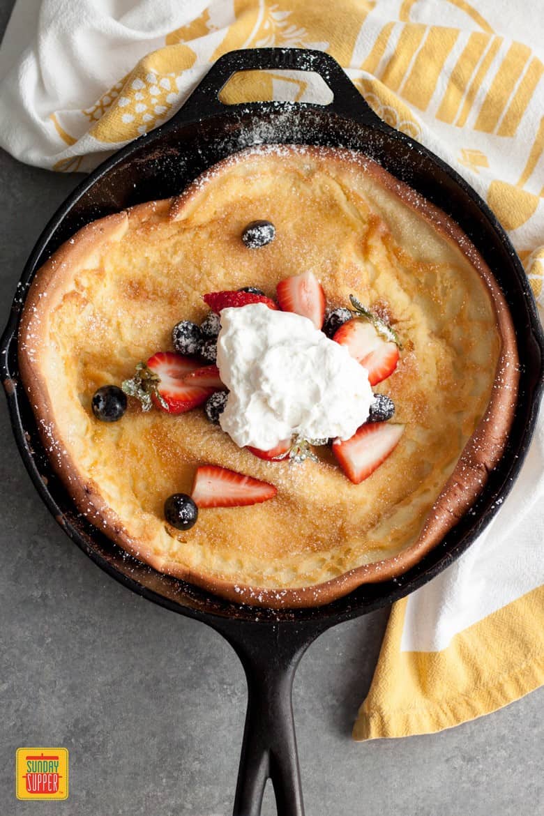 Berries and Cream Dutch Baby topped with whipped cream in a cast iron skillet