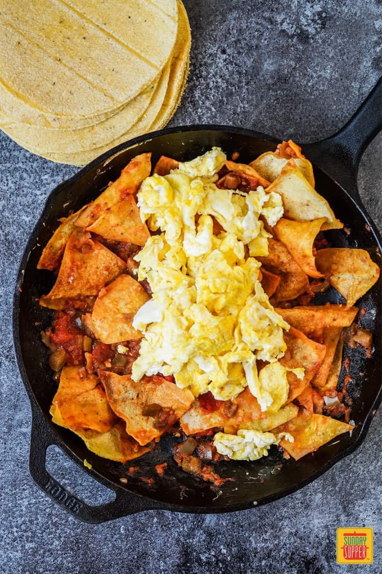 Adding eggs to Chilaquiles Rojos in a cast iron skillet