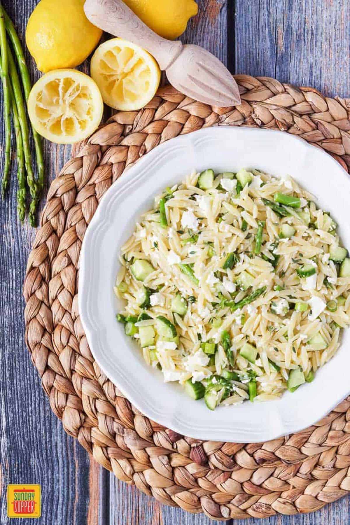 Lemon orzo pasta salad in a large white bowl with squeezed lemons on the side