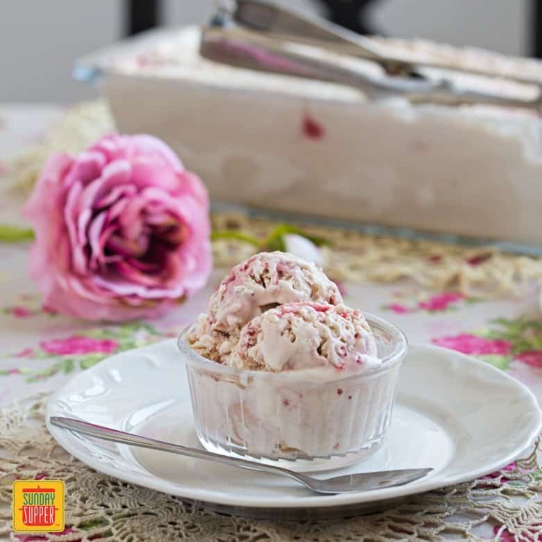 No churn banana raspberry ice cream in a clear dish on a white plate with a spoon