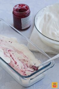 Preparing No Churn Banana Raspberry Ice Cream by mixing the base and the raspberry jam in the freezing container