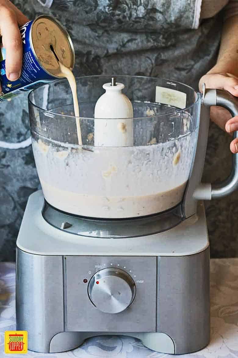 Making No Churn Banana Raspberry Ice Cream in a food processor, adding condensed milk