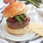 A loaded burger with asparagus spears and bacon on a bun with Parmesan crisps