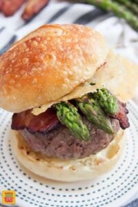 Close up of one of the loaded burgers with spears of asparagus, bacon, and a Parmesan crisp