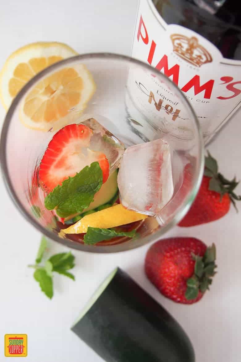 Ice cubes, strawberries, lemon slices, and mint in a glass to make Pimm's Cup Cocktail