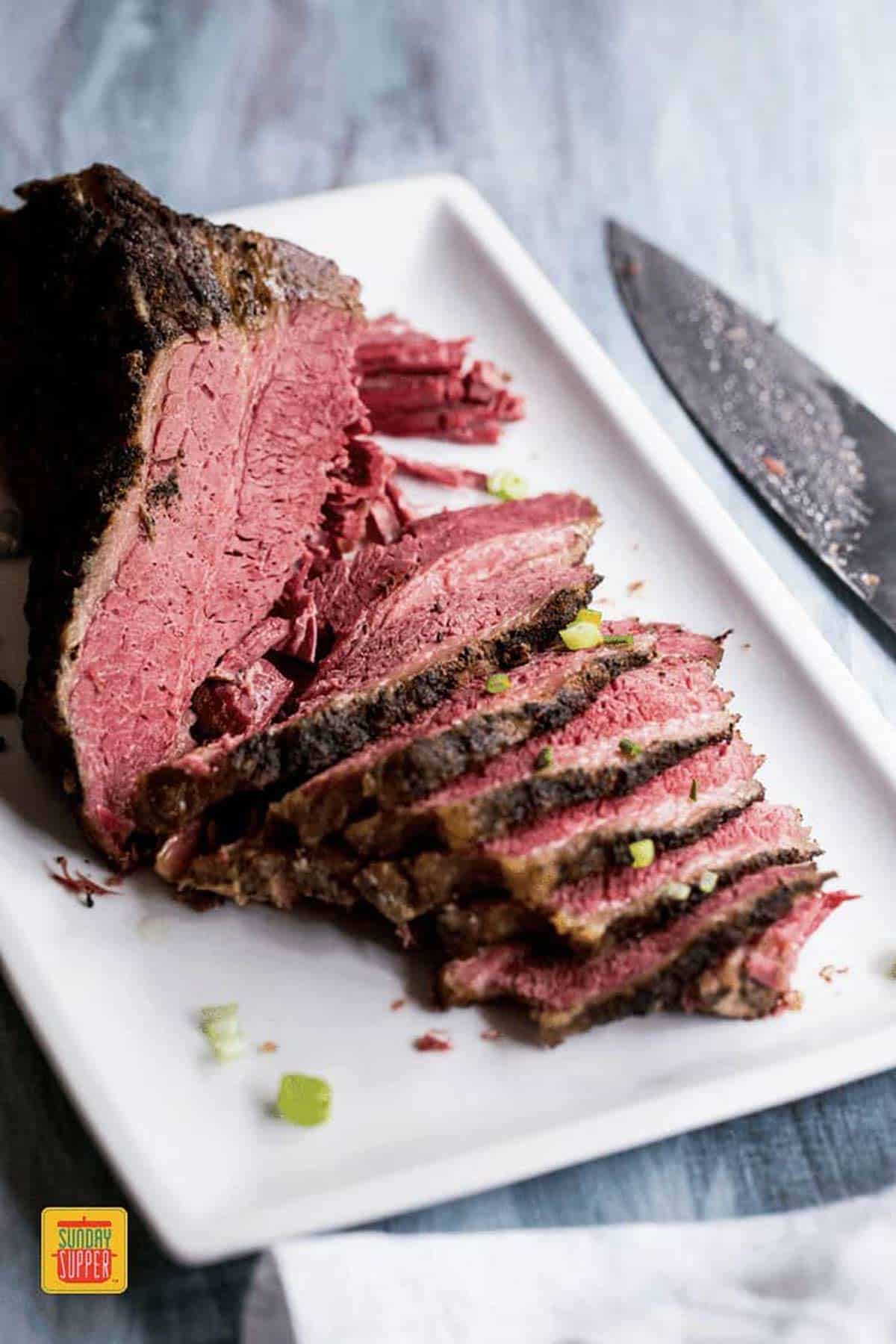 Slow cooker brisket sliced on a white platter next to a knife