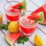 Close up of two glasses of watermelon lemonade with watermelon wedges and lemons on the table