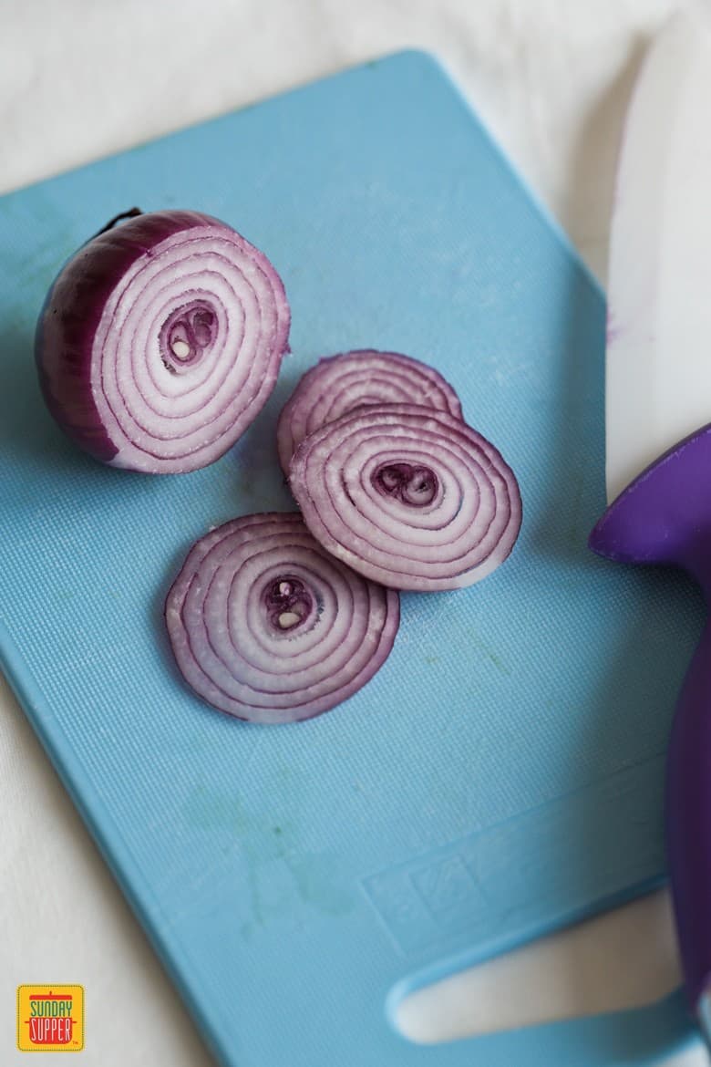 Red onions on a cutting board sliced for the Fresh Vegetable Salad with creamy balsamic Dressing