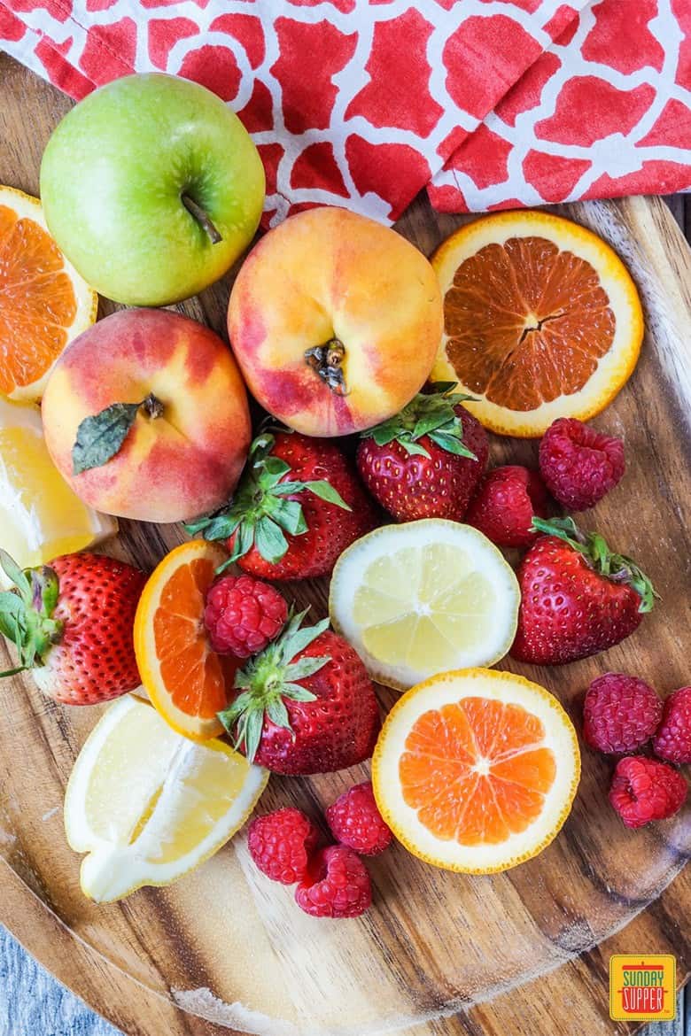 Fresh fruit on a cutting board: peaches, apples, orange slices, strawberries, and lemons