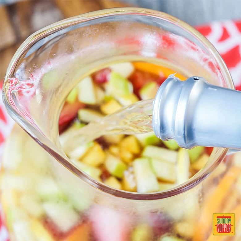 Moscato being poured into a pitcher with fresh fruit slices