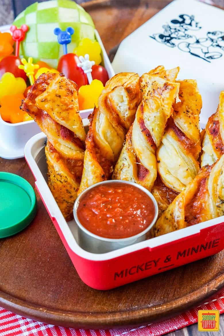 Puff Pastry Pizza Twists in a bento with an apple, grape tomatoes, and bell peppers