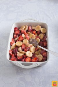 Strawberries and bananas in a white rectangular baking dish mixed with cornstarch and sugar