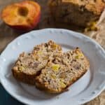 Two slices of Healthier Peach Bread on a plate with peaches and the loaf on the side