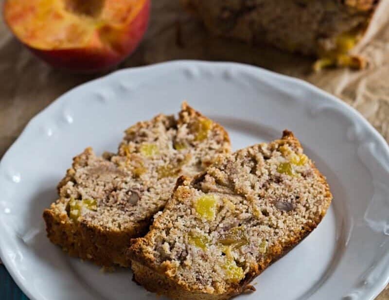 Two slices of Healthier Peach Bread on a plate with peaches and the loaf on the side