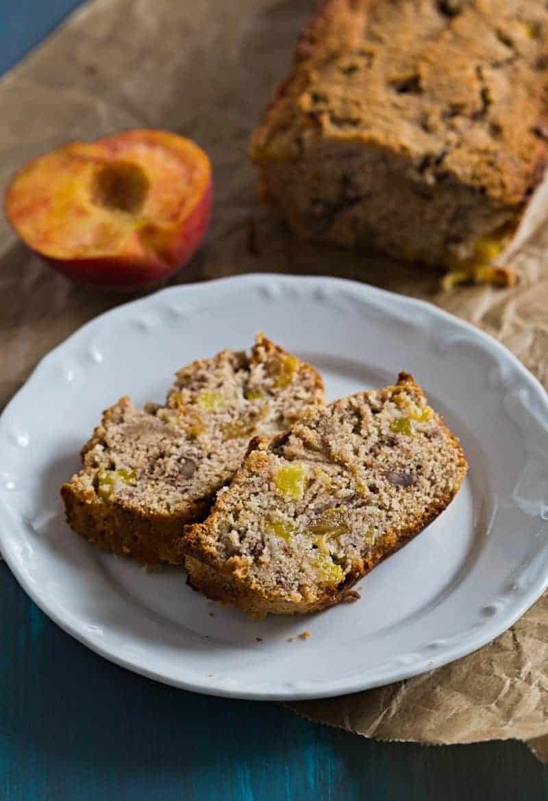 Two slices of Healthier Peach Bread on a plate with peaches and the loaf on the side