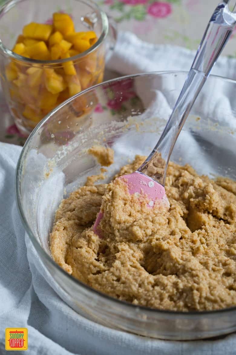 Creating the batter for healthy peach bread in a glass bowl with a rubber spatula