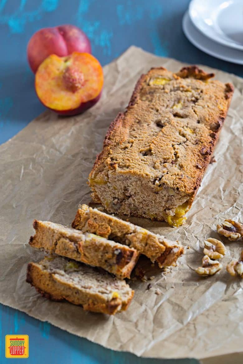 Healthy Peach Bread cut on a blue wooden table with peaches and walnuts on the side