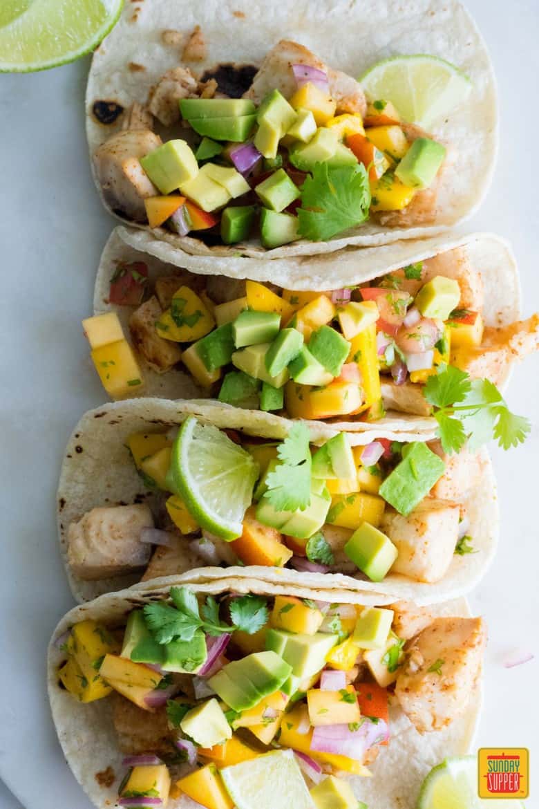 four fish tacos with peach salsa lined up together on white board