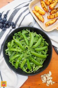 snap peas layered on arugula in bowl