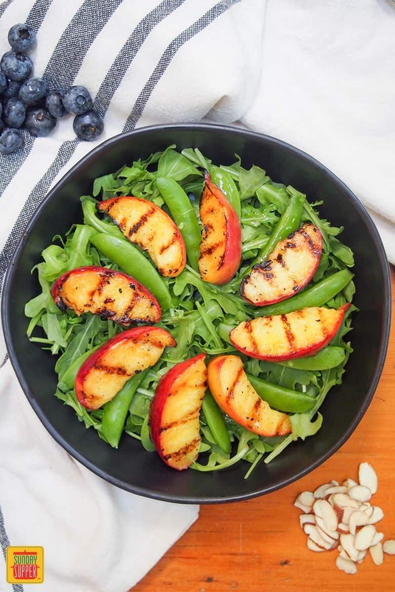 grilled peaches layered on salad in bowl