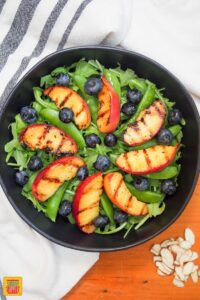 adding blueberries to grilled peaches salad