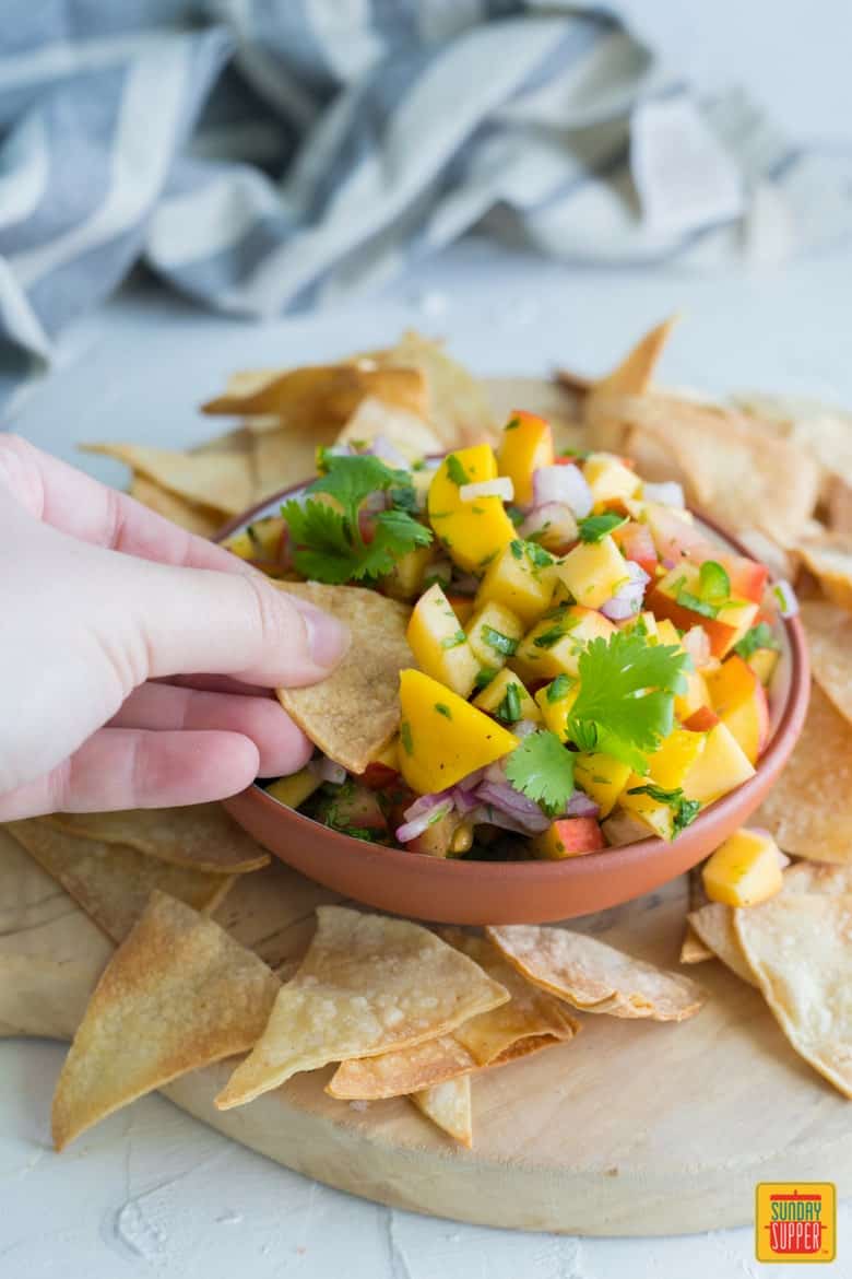 hand reaching out with a tortilla chip to get peach mango salsa
