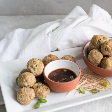 Thai chicken meatballs on a white platter with a cup of dipping sauce in the center