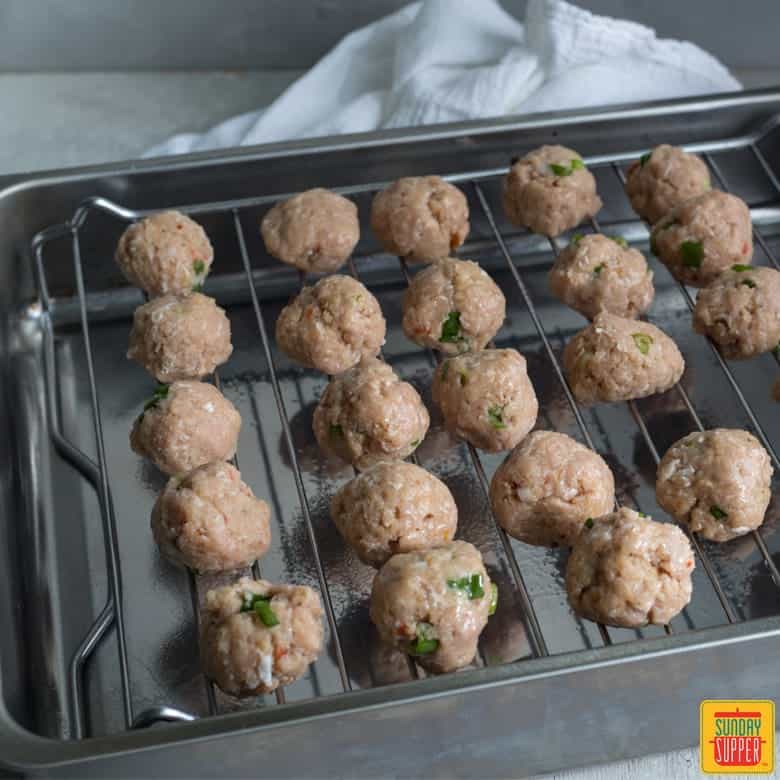 raw thai chicken meatballs rolled into balls, on wire rack placed in baking tray