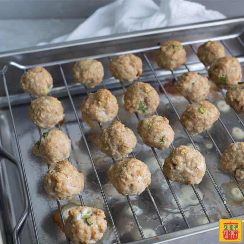 cooked thai chicken meatballs on a wire rack placed in baking tray