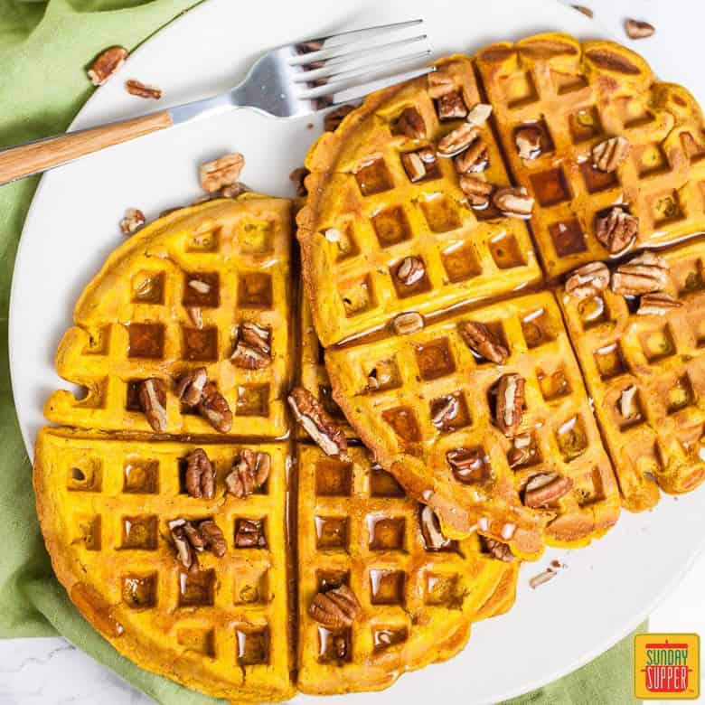 Two pumpkin waffles on a white plate with a fork and syrup on top