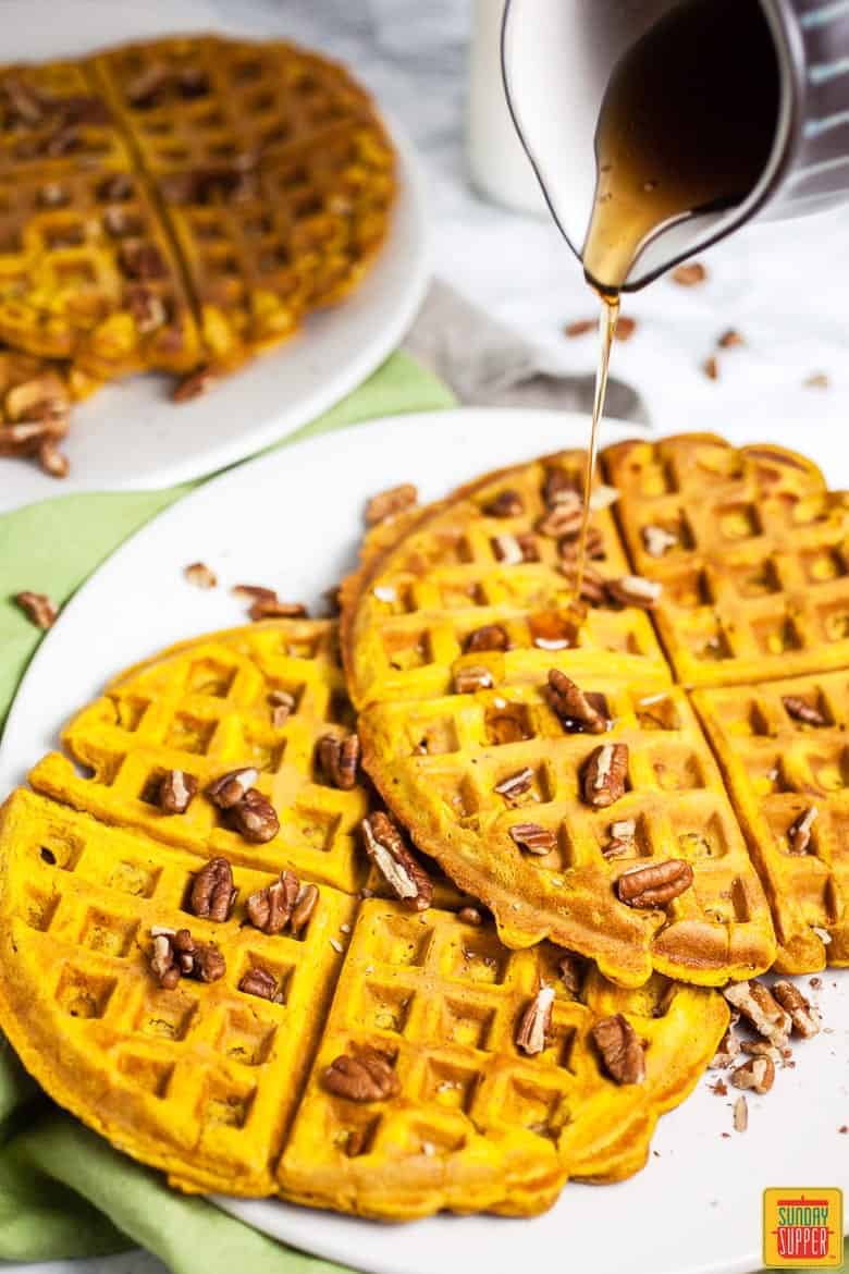 Pouring syrup onto two pumpkin waffles on a white plate