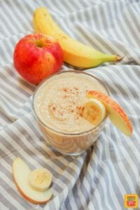 apple banana smoothie in a cup with an apple and banana slice on the rim of the cup