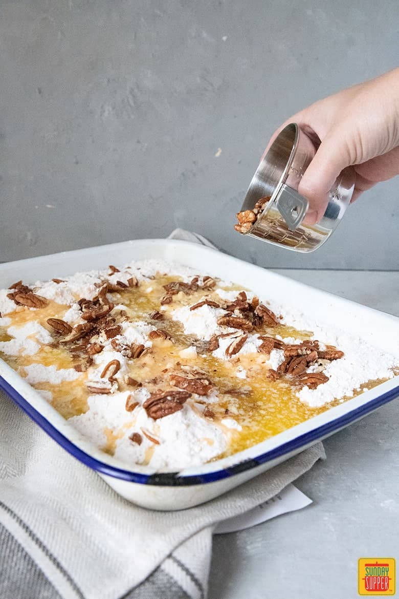 pecans being poured over pumpkin crunch recipe ingredients in enamel pan