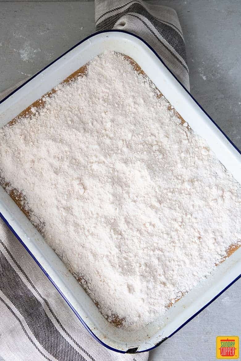 Yellow cake mix spread over pumpkin crunch cake mixture in a white baking dish