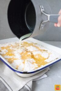 butter being poured from a saucepan into pumpkin crunch recipe ingredients in white and blue enamel dish