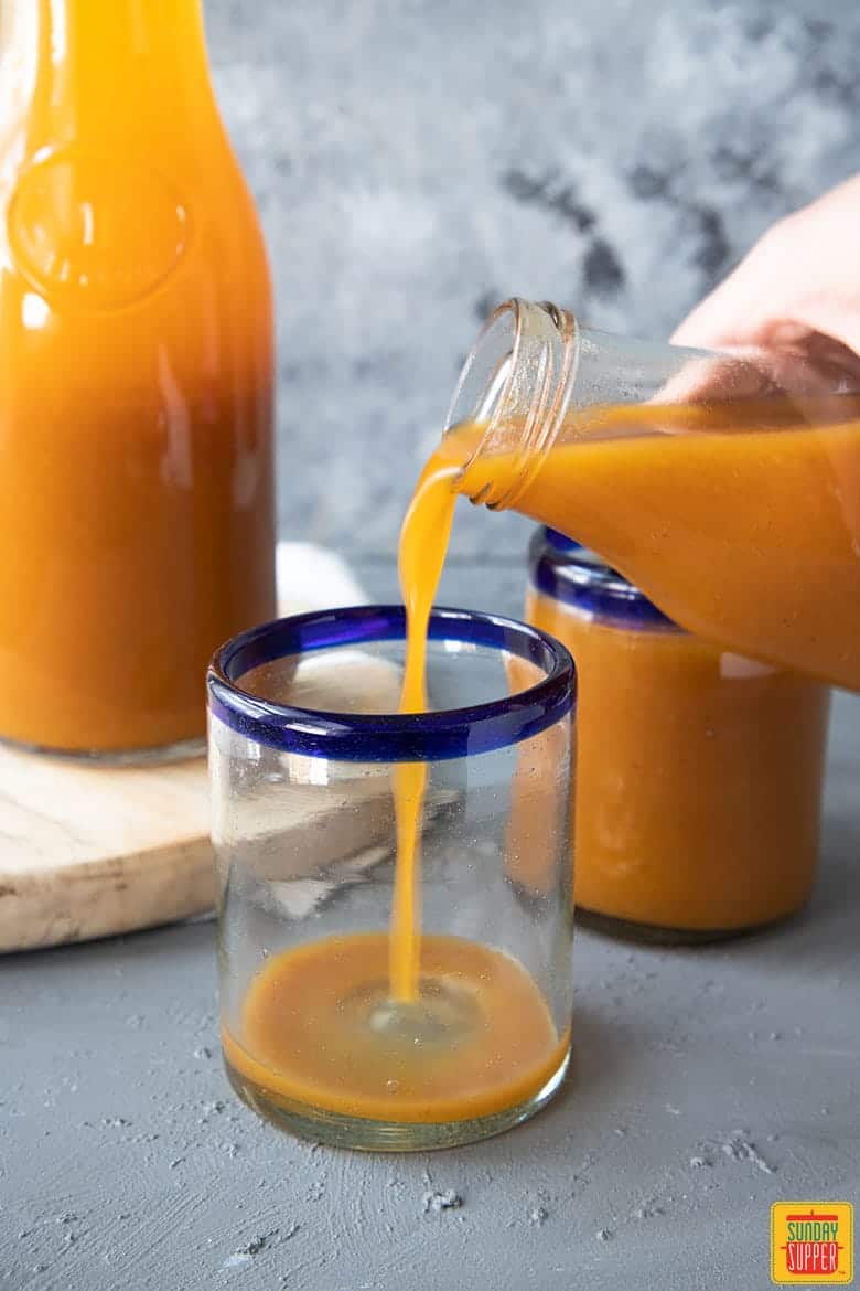 hand pouring pumpkin juice into clear glass with blue rim