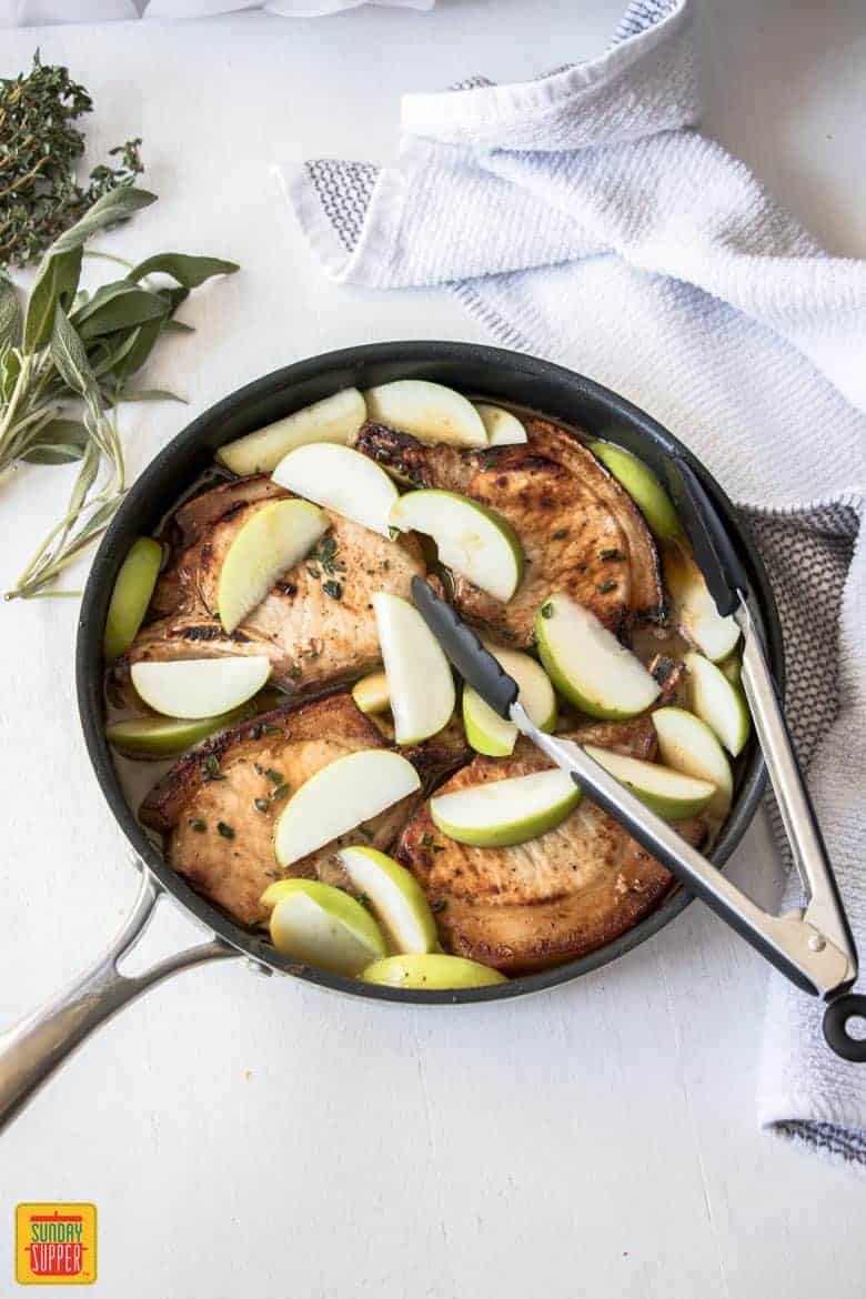 Baked apple pork chops in a skillet with fresh apple slices, still cooking