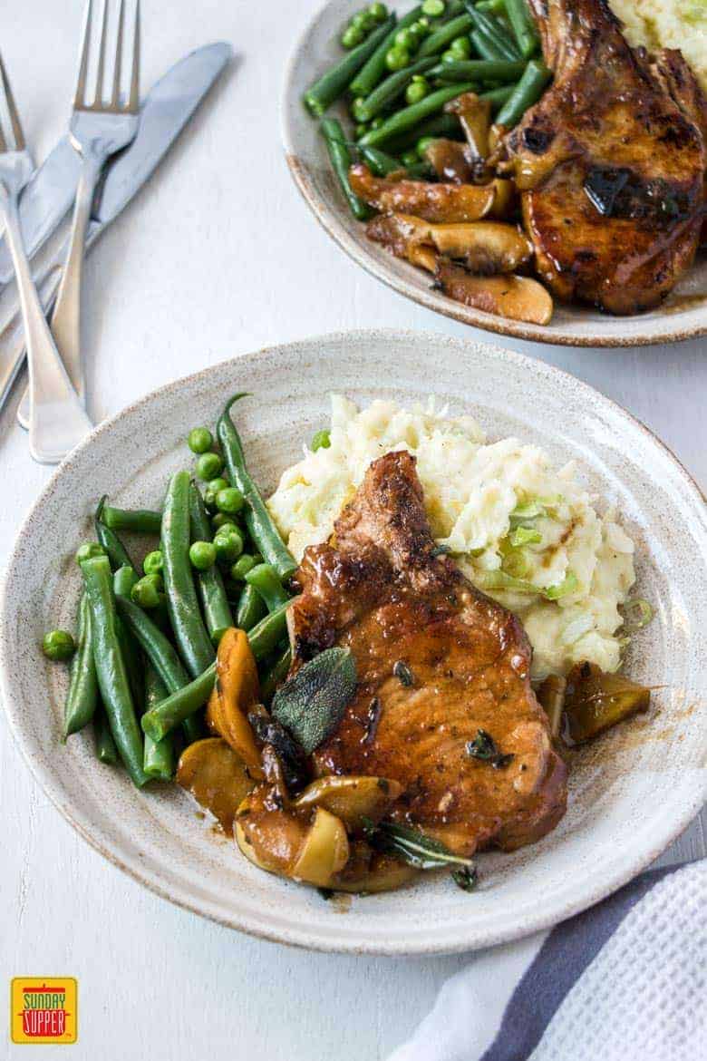 Baked Apple Pork Chops served on white plates with mashed potatoes and green beans