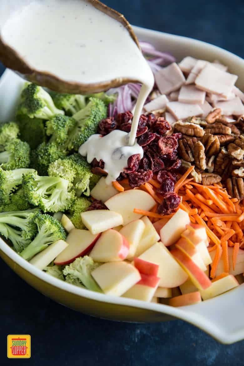 Pouring dressing over Broccoli Apple Salad with turkey