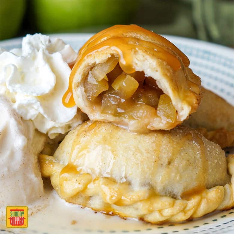 Caramel apple empanadas split in half to show filling with a side of whipped cream and ice cream on a white plate