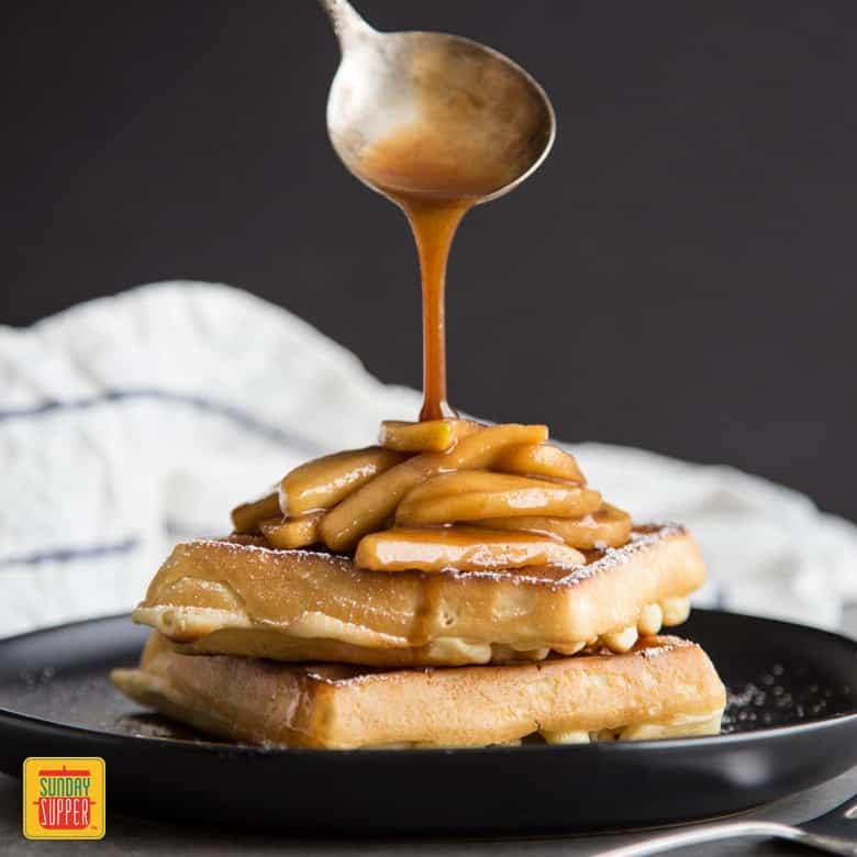 Sauteed Apples served over waffles with a spoon over top drizzling on sauteed apple sauce
