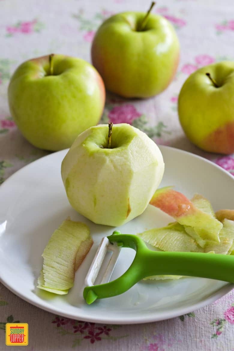 A peeled apple next to a y-peeler on a white plate