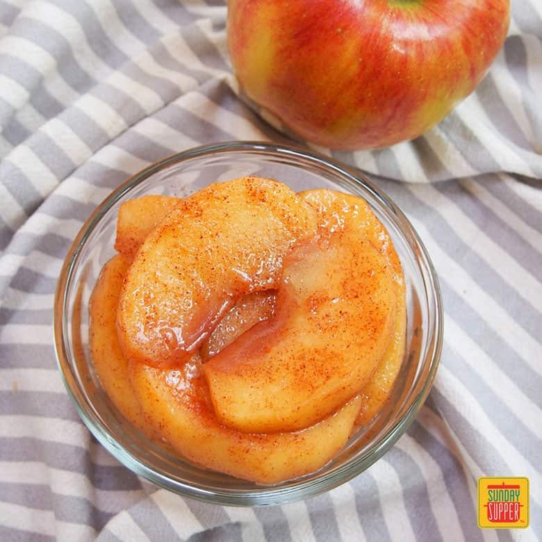 Stewed apples in a glass container next to a fresh apple