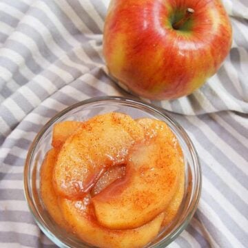 Stewed apples in a glass container next to a whole apple