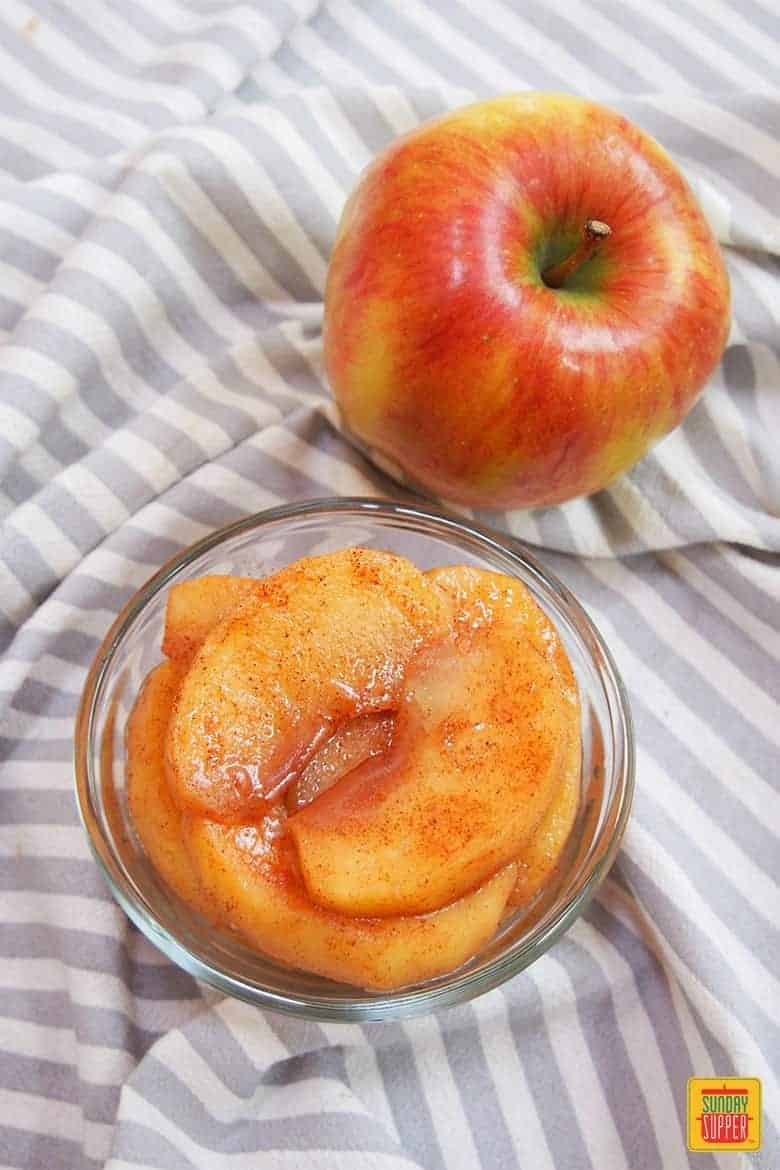 Stewed apples in a glass container next to a whole apple