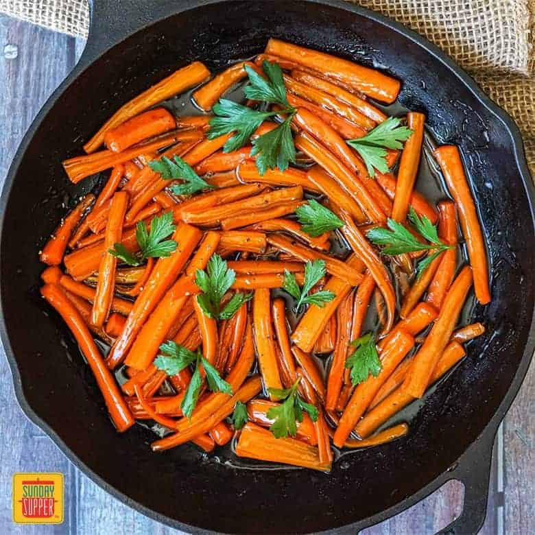 Brown Sugar Glazed Carrots with a sprinkling of fresh parsley in a cast iron skillet