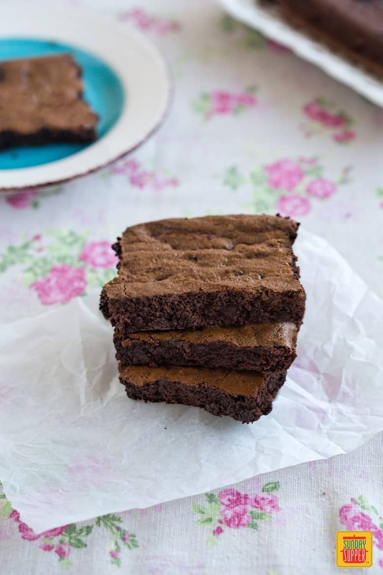 Three stacked Gluten Free Fudge Brownies on a piece of parchment paper