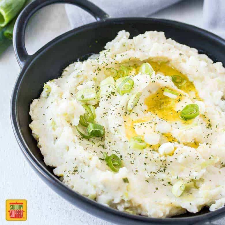 Irish Mashed Potatoes - Colcannon in a black dish with melted butter and scallions