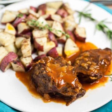Instant pot pot roast on a white plate with potatoes and herbs