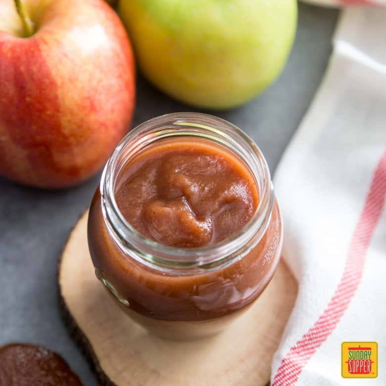 Slow Cooker Apple Sauce in a jar next to fresh apples